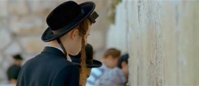 A Hassidic (ultra-orthodox) Jewish boy/man with peyot/peyas (religiously uncut portions of the hair before the ears) and Tefilim (religious boxes with Hebrew scrolls within strapped to the forehead and arm) davening (praying) before the Kotel (Western Wall, Wailing Wall, etc) in Jerusalem, Israel.